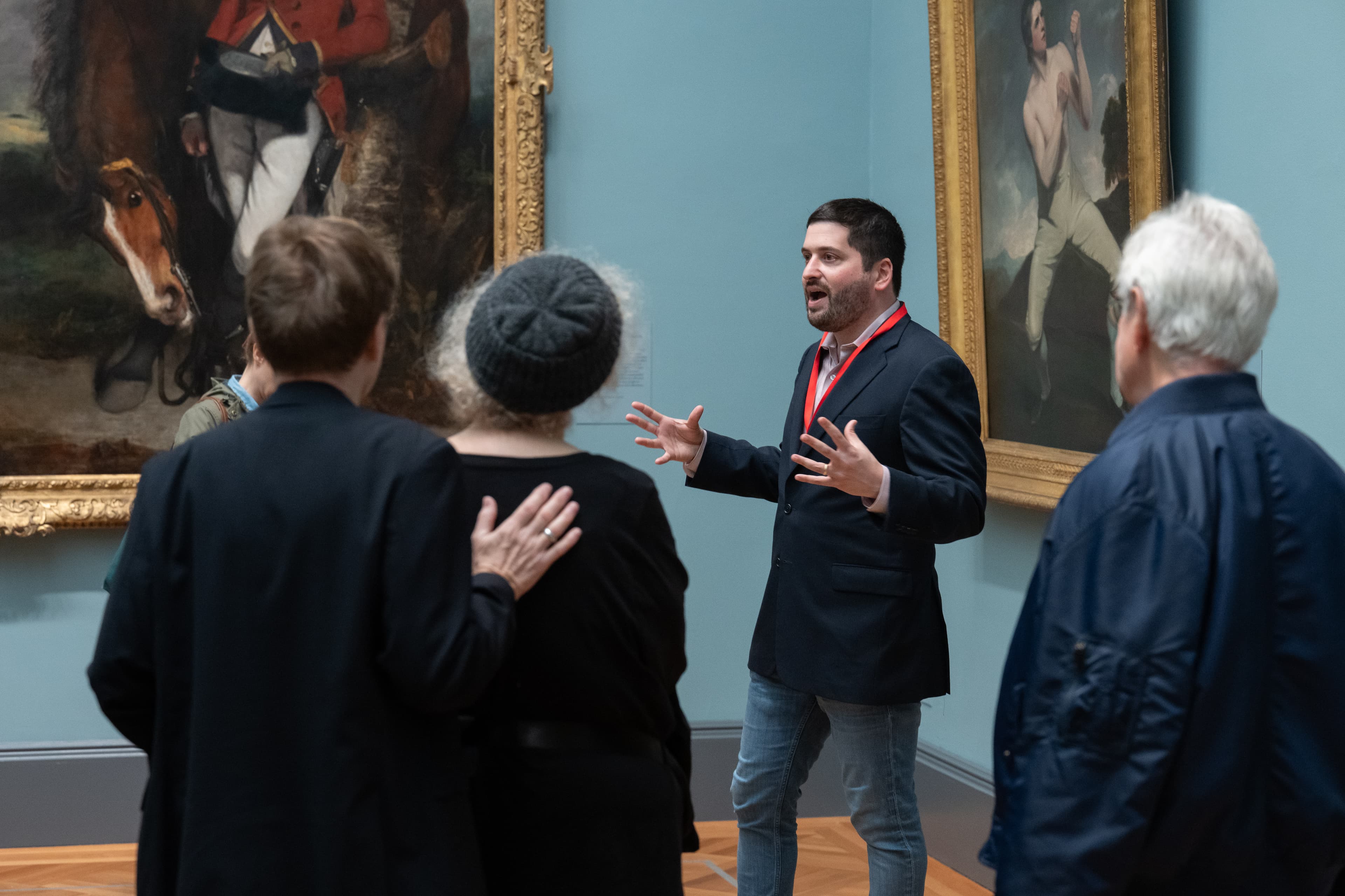 Una foto de una charla. Rodeada por una exposición, un ponente interactúa con un pequeño grupo.  